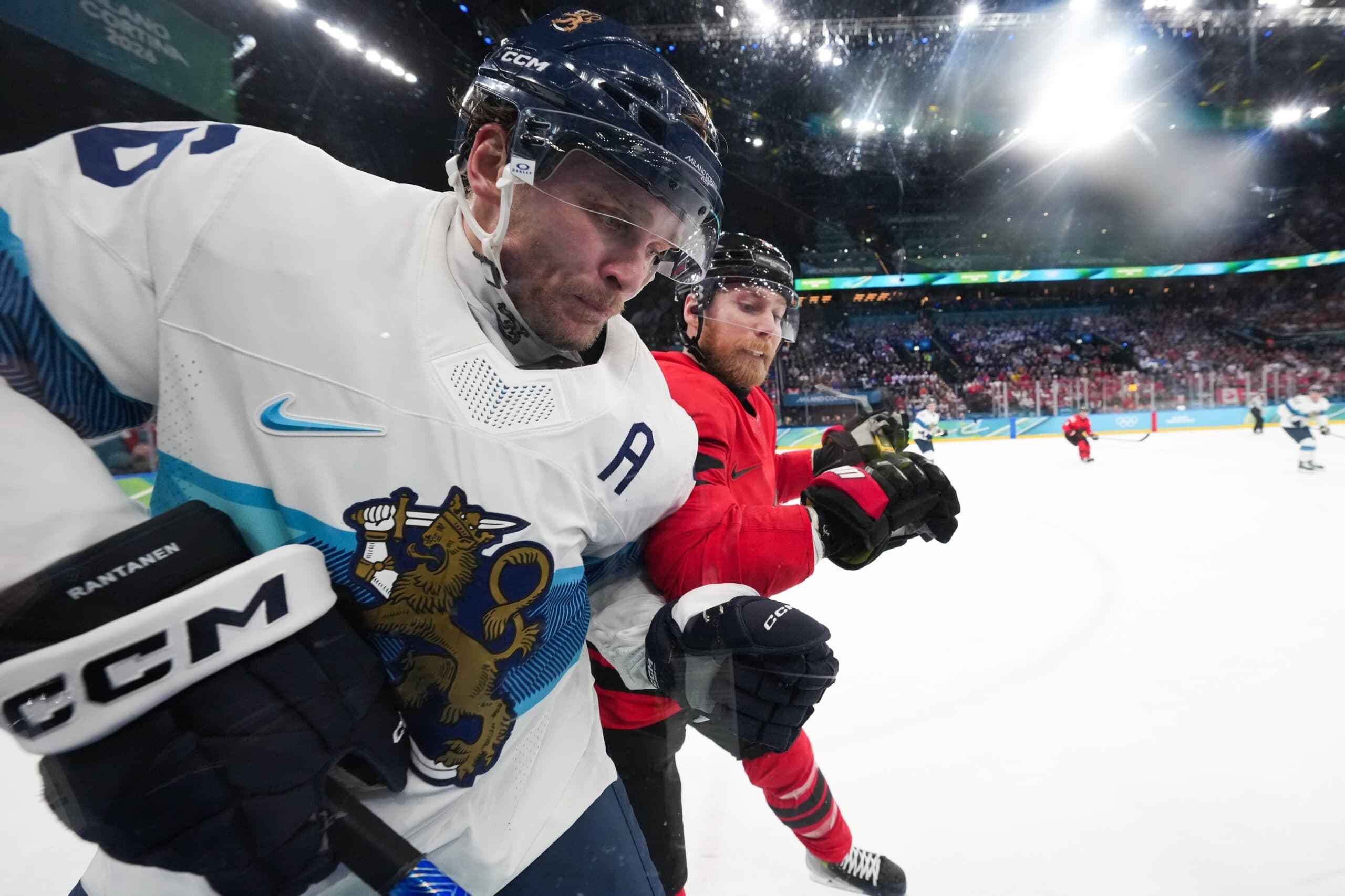 Sam Bennett (9) of Canada checks Mikko Rantanen (96) of Finland into the boards during the second period in a men's ice hockey semifinal during the Milano Cortina 2026 Olympic Winter Games at Milano Santagiulia Ice Hockey Arena.